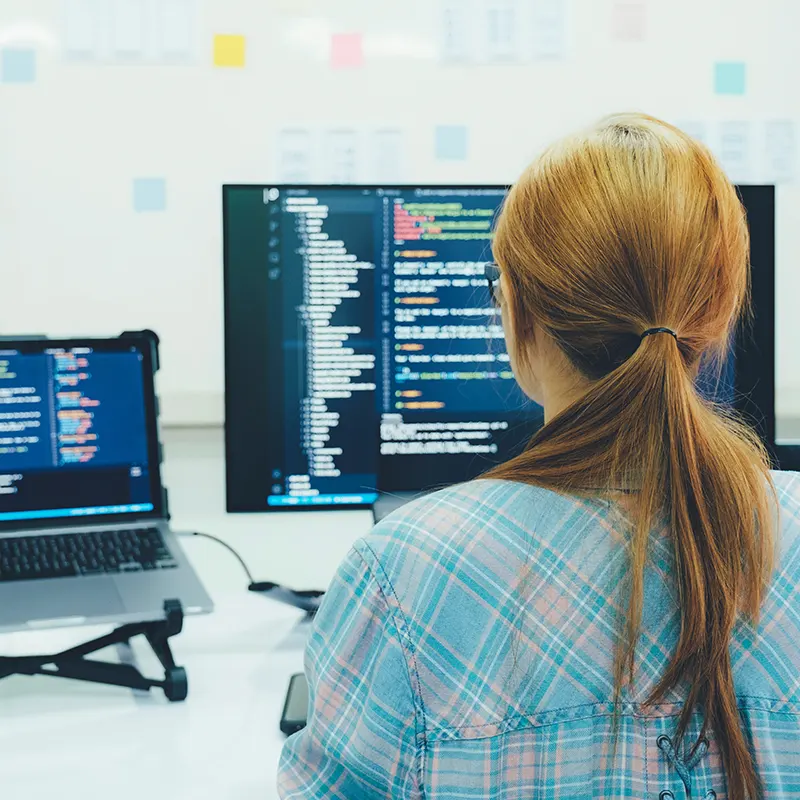 Programmeur werkt aan maatwerk software met code op meerdere schermen
